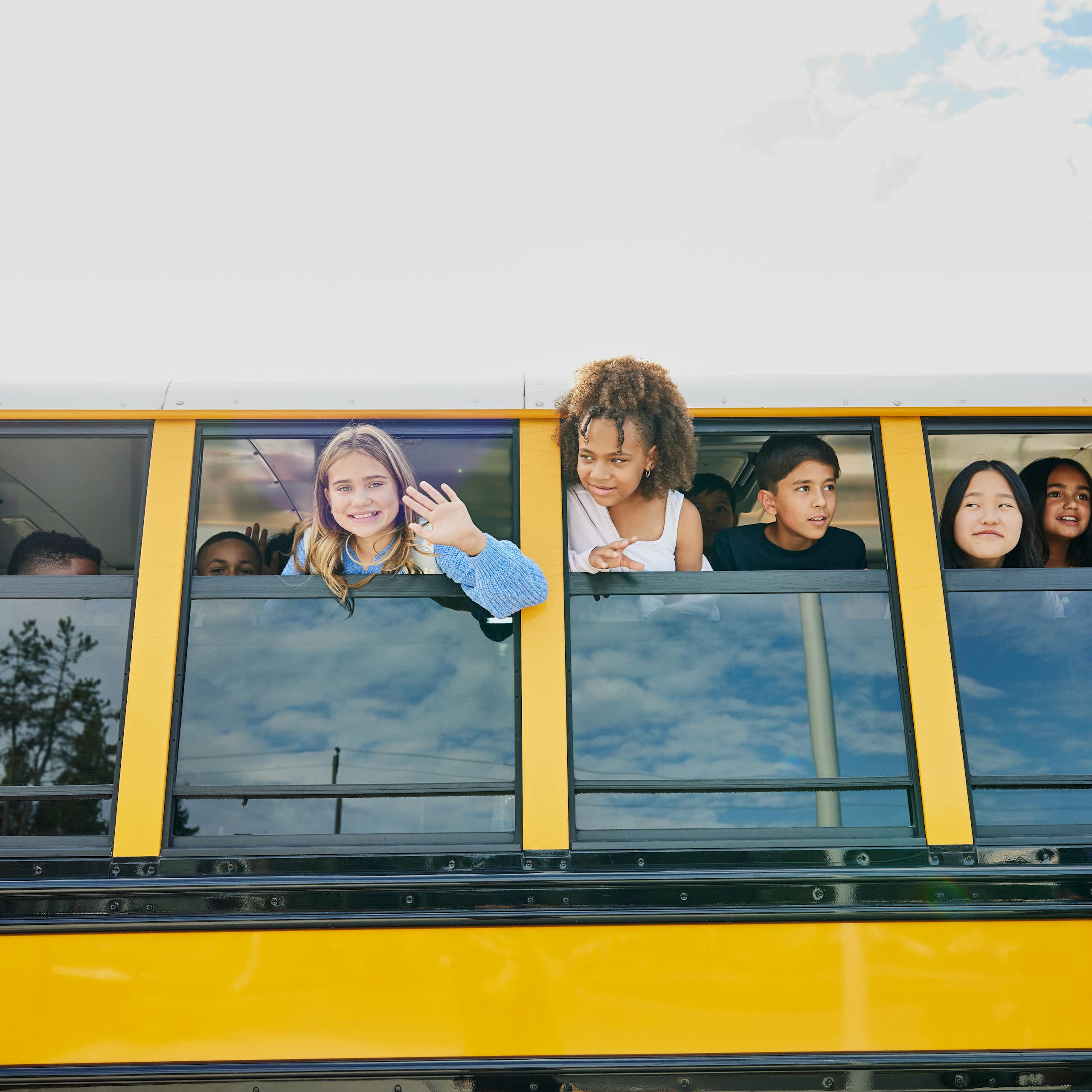 Children stick their heads out of a stopped yellow school bus and waving.