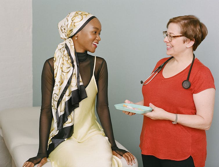 A health care provider holds a tray with a syringe and talks to a young girl at a clinic