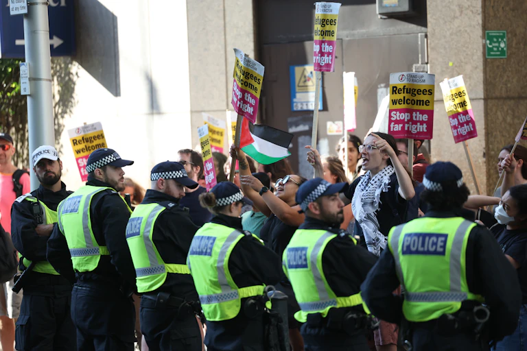 A row of police holding back a group of activists with signs reading 'refugees welcome, stop the far right'