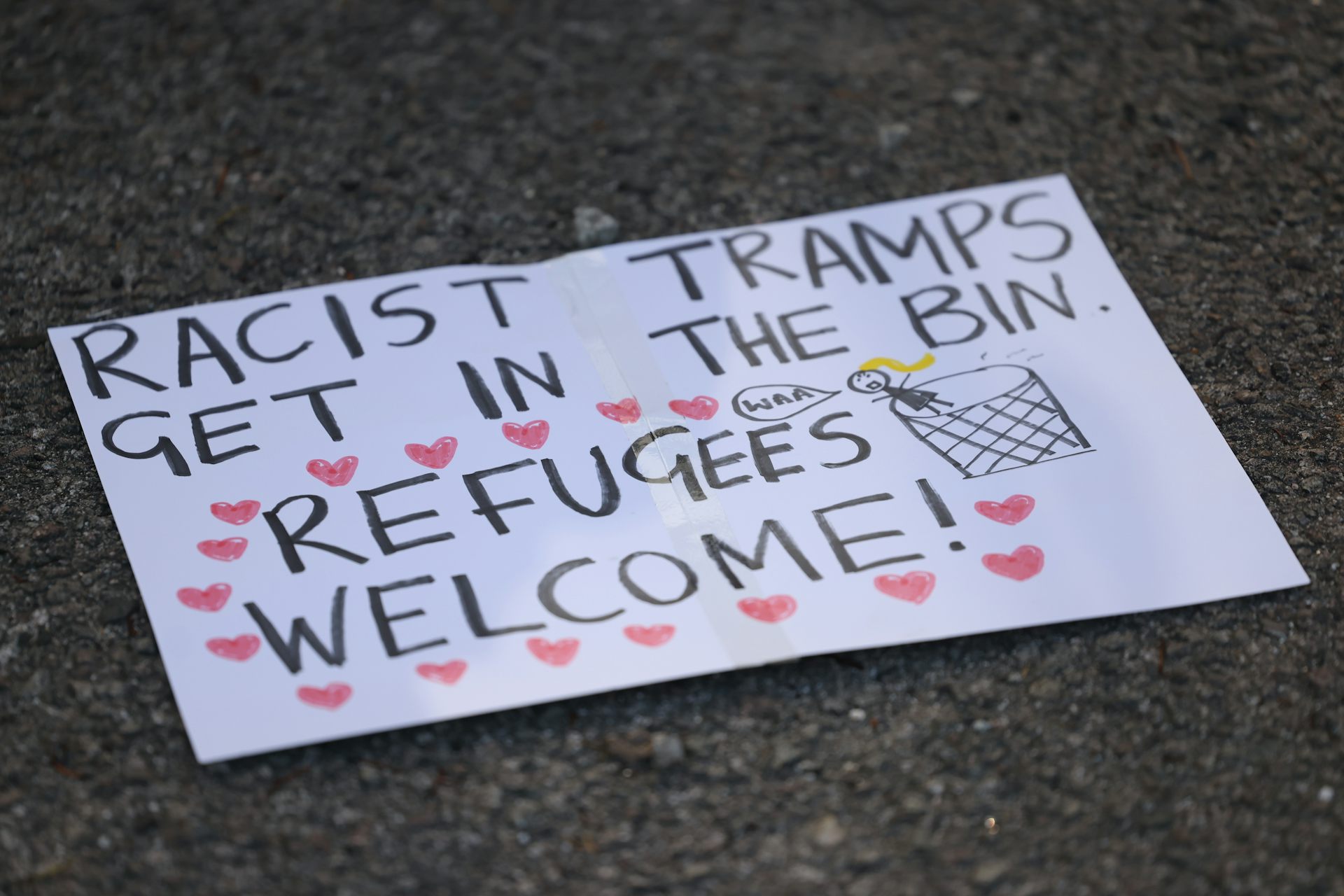 A protest sign on the ground that reads 'racist tramps get in the bin, refugees welcome'