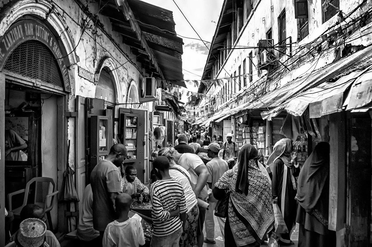 A black and white photo of a bustling market street lined by old buildings.