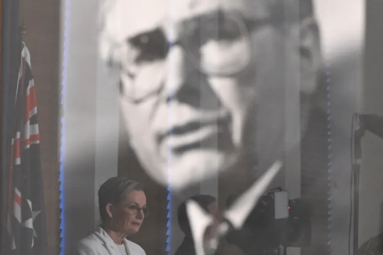 Sussan Ley gives a speech within the reflection of John Howard's portrait