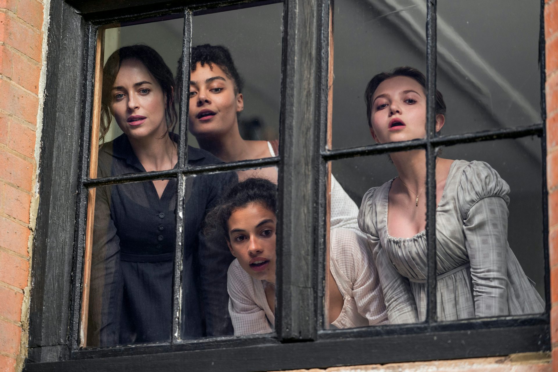 Four women eagerly looking out of a window at the street below