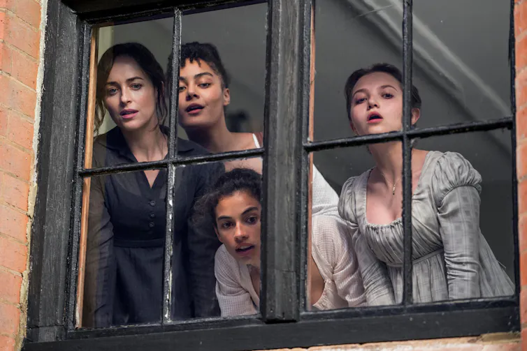 Four women eagerly looking out of a window at the street below