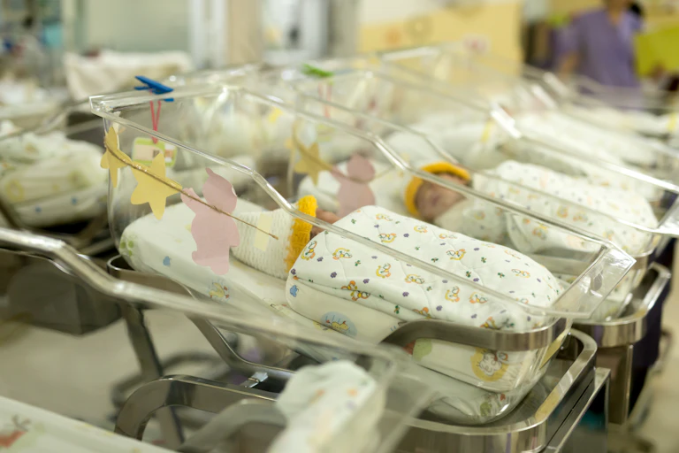 Une rangée de bébés dans des berceaux transparents, à l'intérieur d'une maternité.