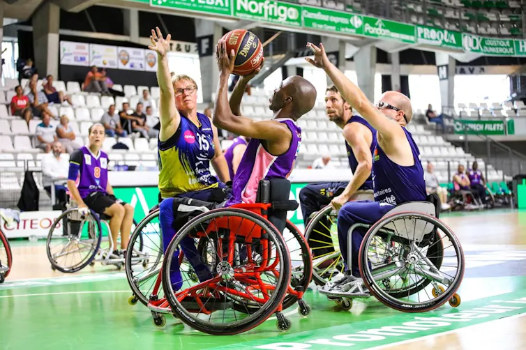 A group of male and female Para athletes in wheelchairs, one aiming to shoot, the others trying to block with their outstretched arms.