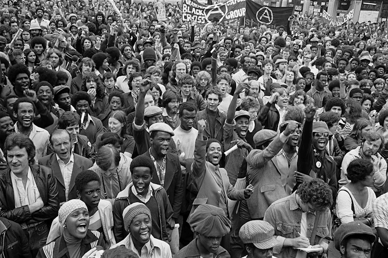 A group of mainly black young men on a protest march cheering and waving, looking happy.