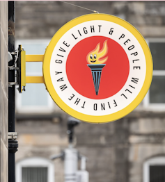 A yellow and red street sign that says Give Light And People Will Find The Way.