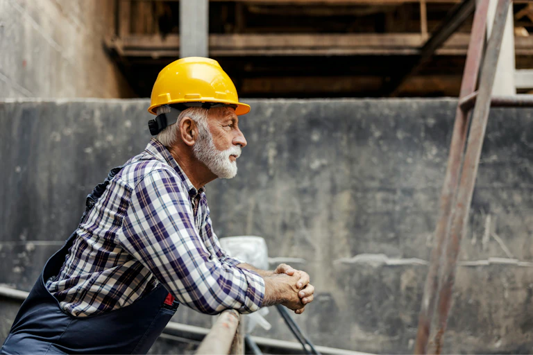 Un homme âgé en habit de construction regarde un chantier.