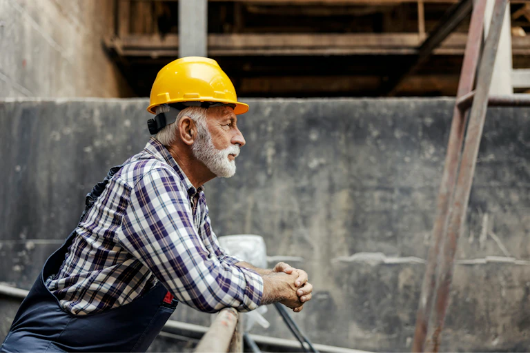 Un homme âgé en habit de construction regarde un chantier.