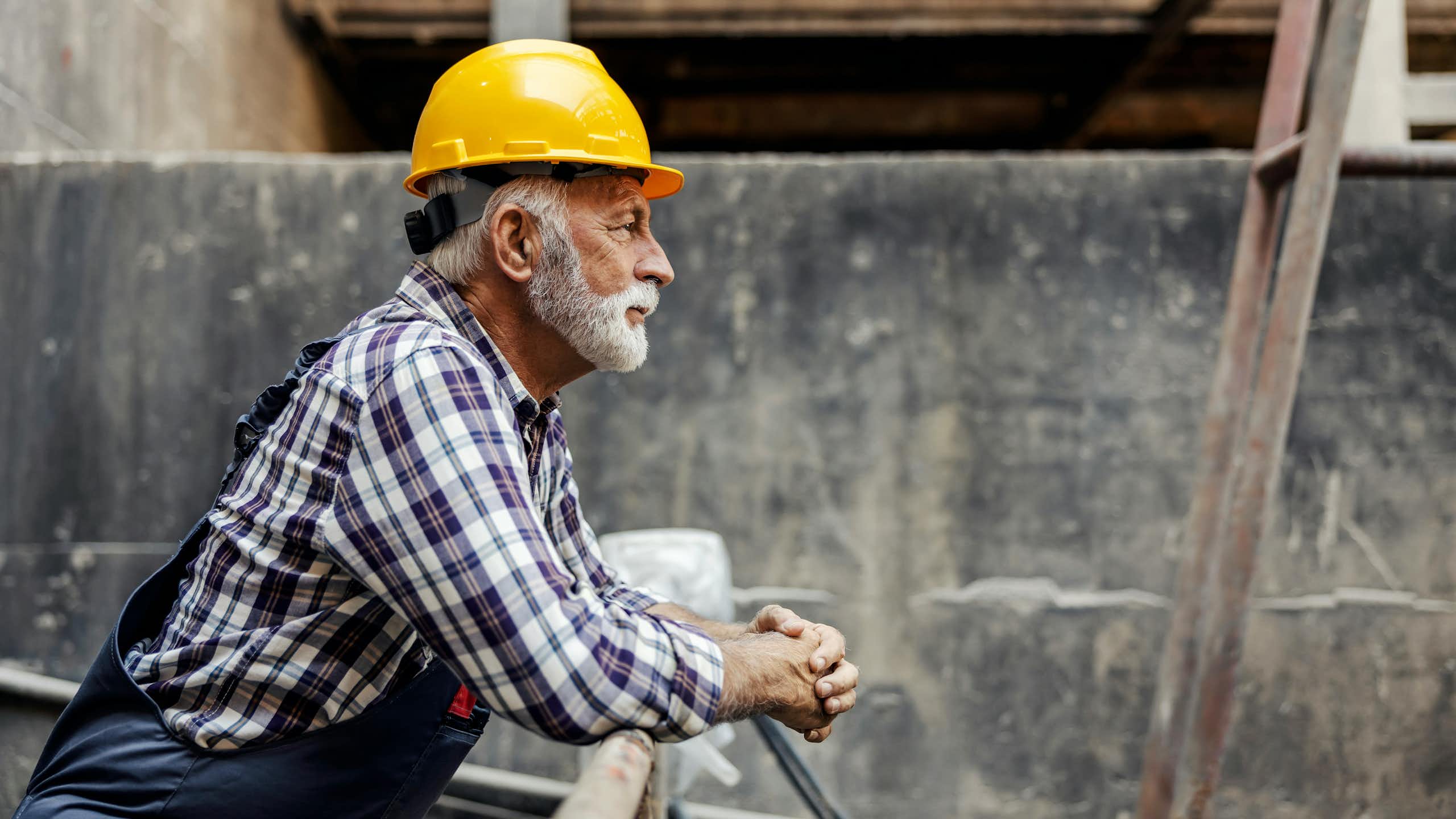 Un homme âgé en habit de construction regarde un chantier.