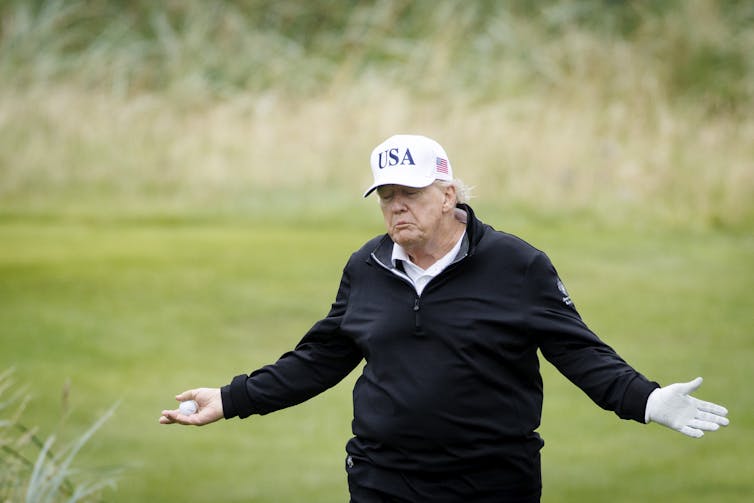 Donald Trump shrugging, holding a golf ball.