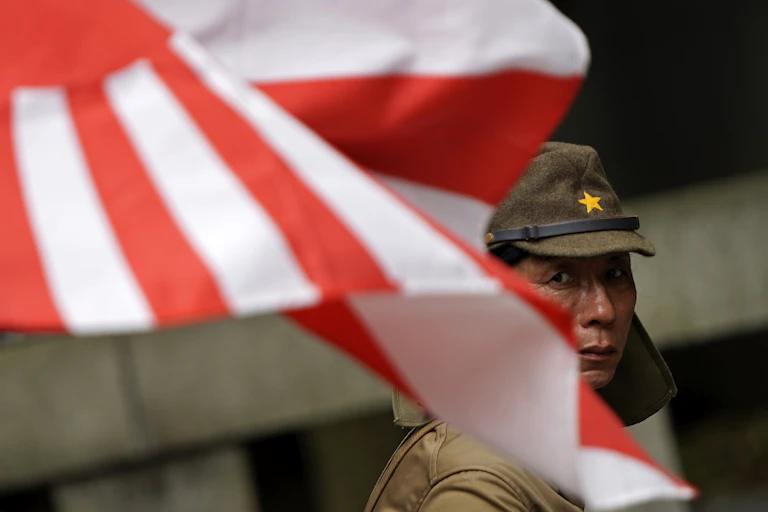 A Japanese man dressed as an imperial army soldier stands behind Japan's imperial flag.