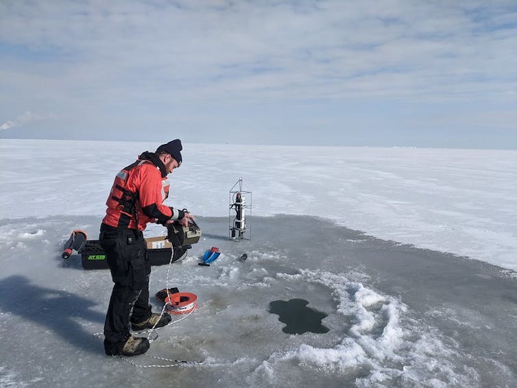 El clima más cálido está provocando la desaparición del invierno en los Grandes Lagos de América del Norte 2 un hombre vestido de invierno se encuentra en un lago congelado con instrumentos de muestreo.