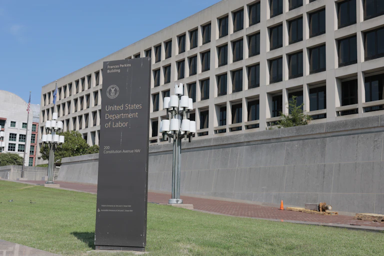 Four story cement building with freestanding with U.S. Department of Labor sign on the lawn in the foreground