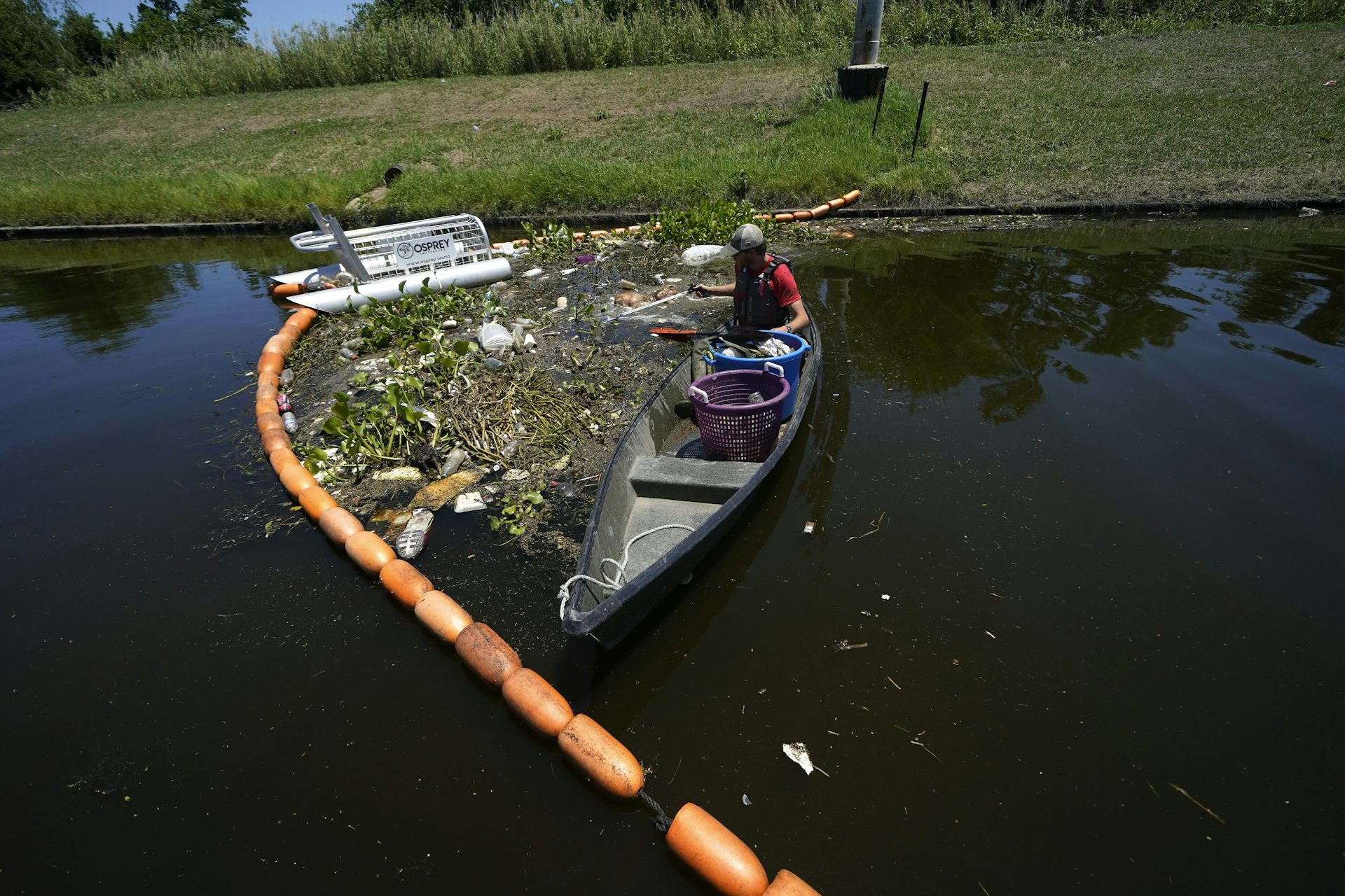 Hombre en un pequeño bote cerca de la basura flotante en un campo de agua junto a una serie de portadores flotantes
