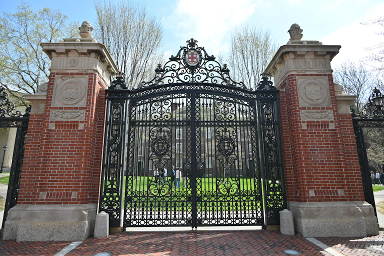 Two large red brick towers stand on either side of a black metal gate that is closed, with a green lawn beyond the gates.