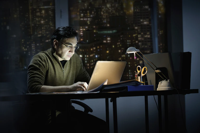 A man in an office building in a city works late at night, when it's dark out.