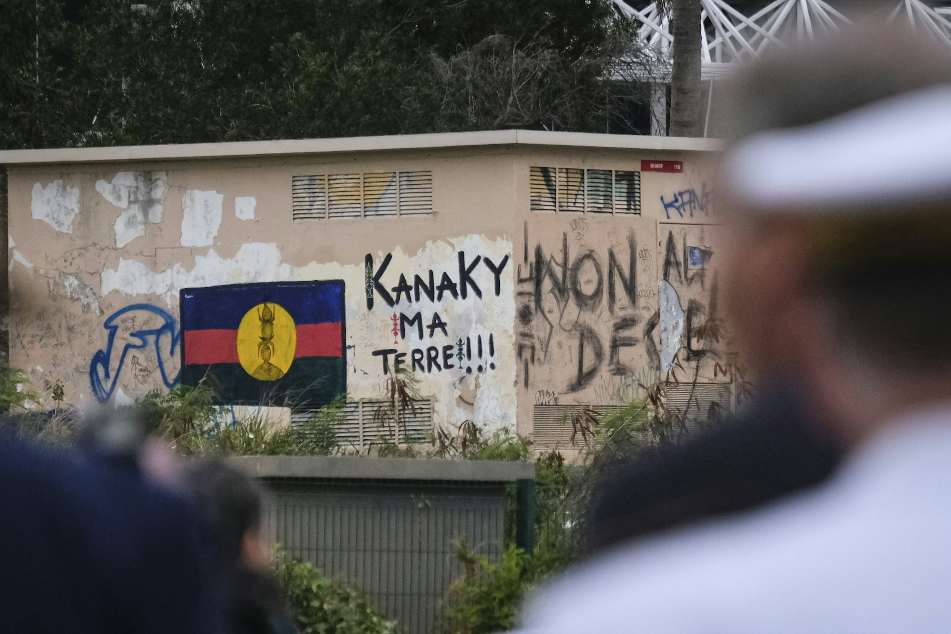 Un homme regarde un graffiti d'un drapeau calédonien à côté d'une inscription « Kanaky, ma terre ! » sur un mur de Nouméa, la plus grande ville de Nouvelle-Calédonie.