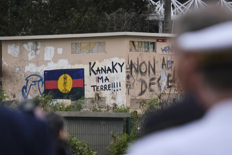 Un homme regarde un graffiti d'un drapeau calédonien à côté d'une inscription « Kanaky, ma terre ! » sur un mur de Nouméa, la plus grande ville de Nouvelle-Calédonie.