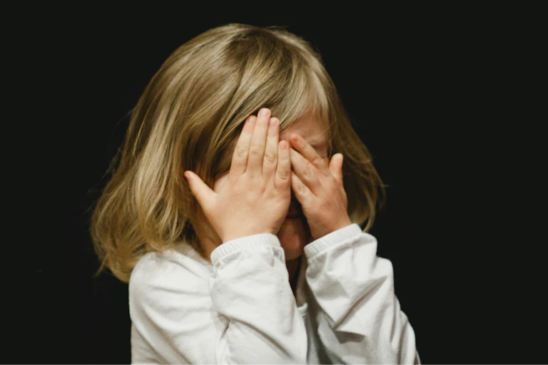 a young girl covers her eyes against a black background