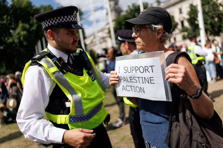 A police officer faces a woman holding a placard that reads 'I support Palestine Action'