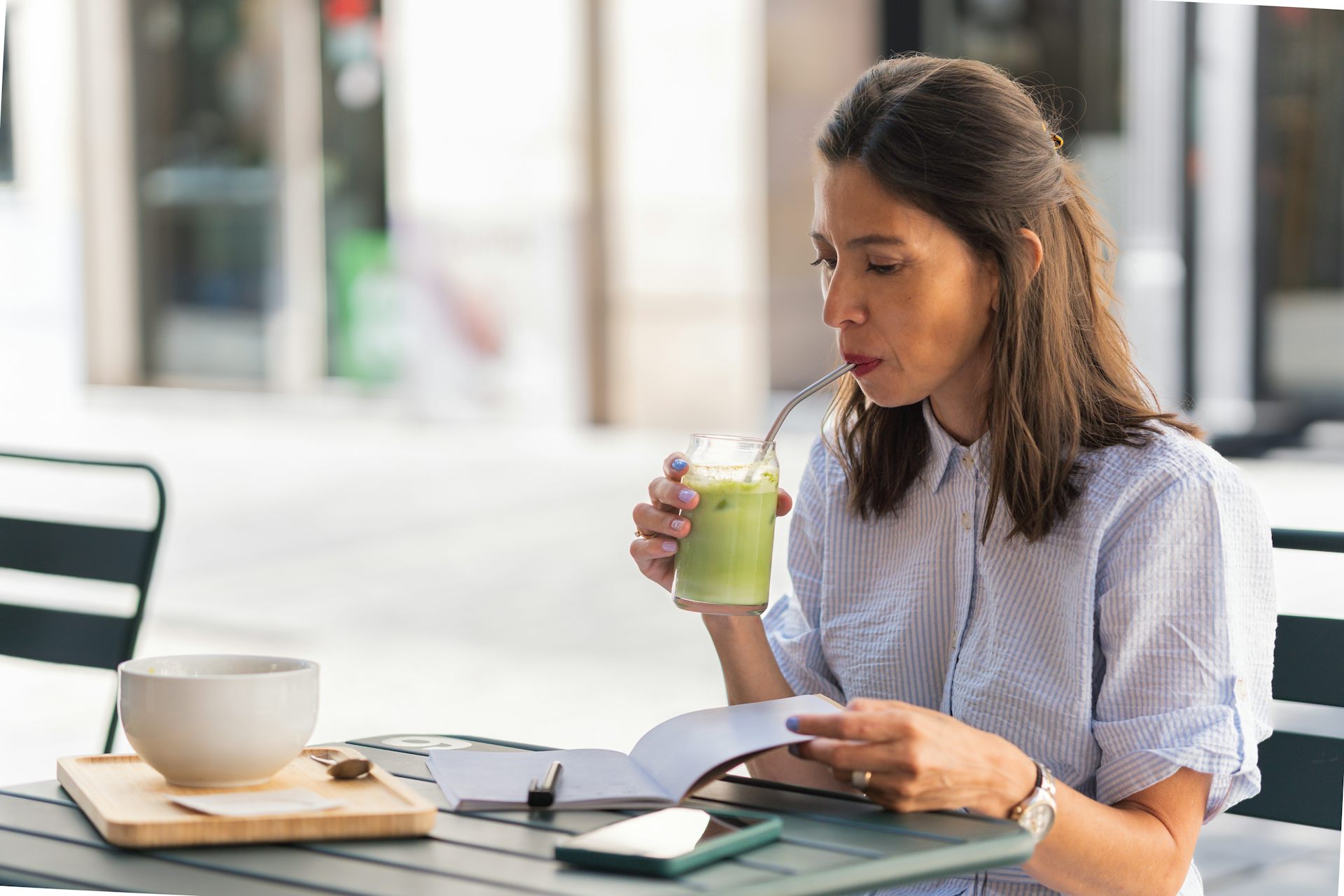 Mujer bebiendo una bebida con pajita y hojeando un cuaderno