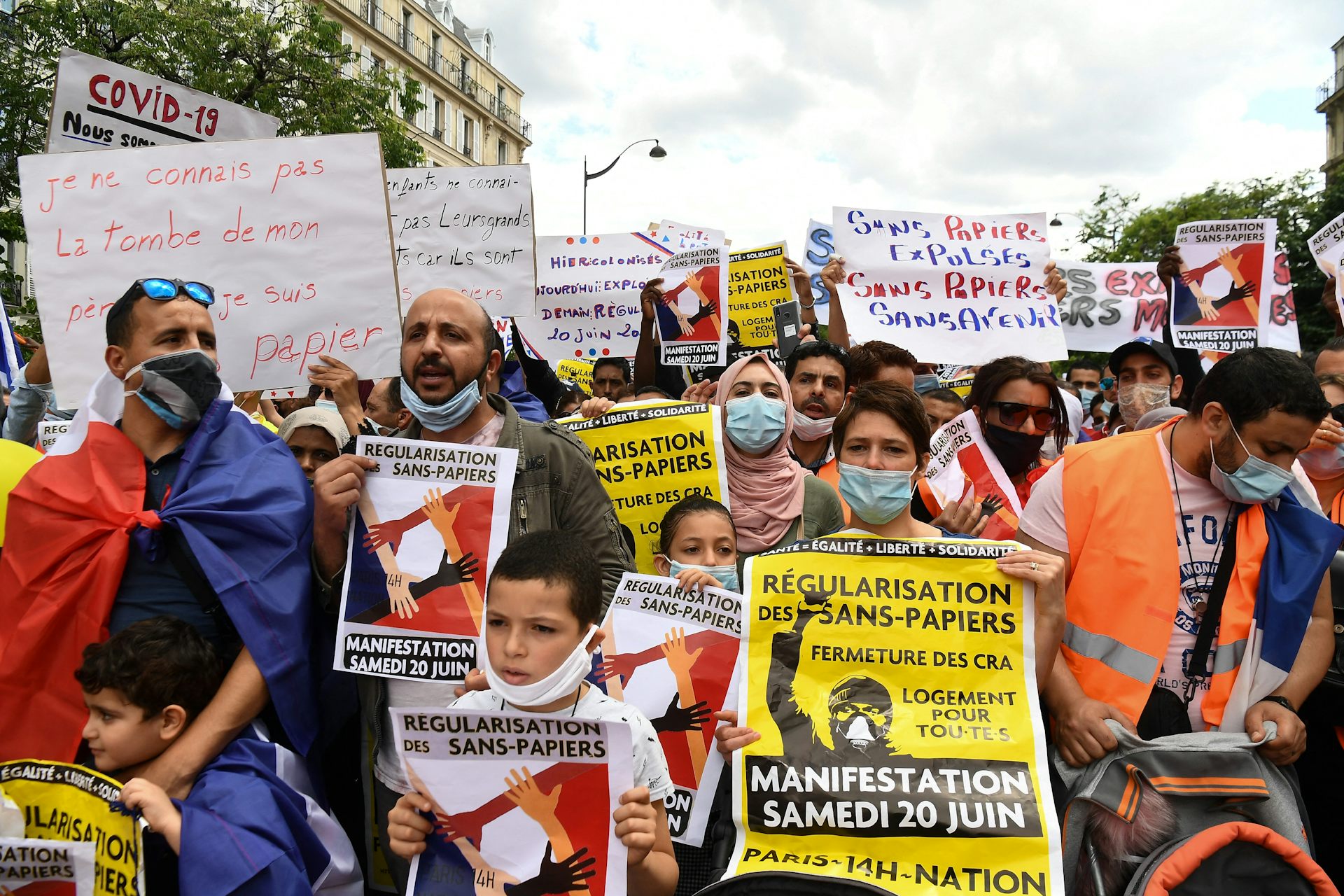 People hold signs with messages, written in French, calling for the regularisation of undocumented immigrants at a protest.