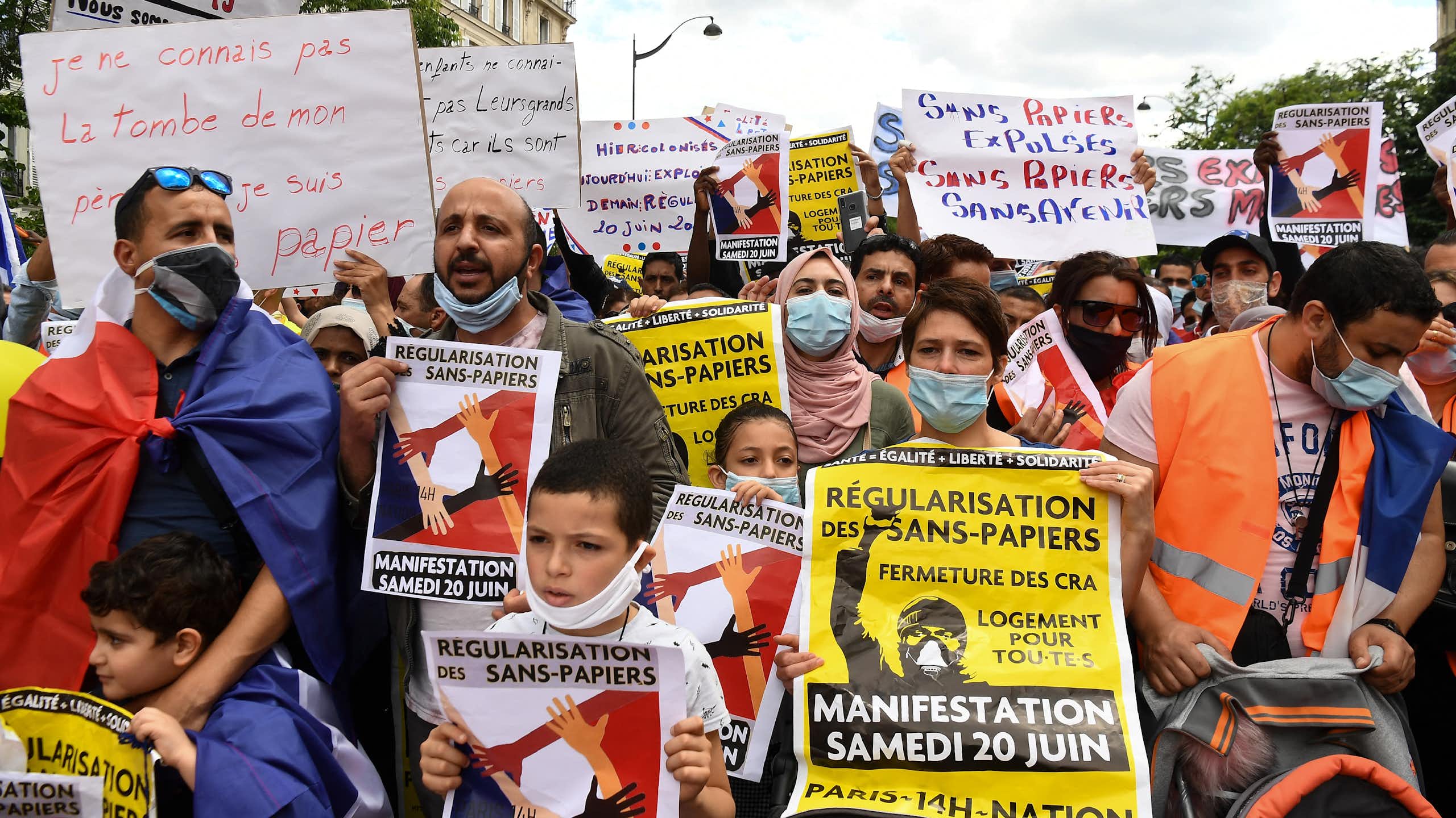 People hold signs with messages, written in French, calling for the regularisation of undocumented immigrants at a protest.