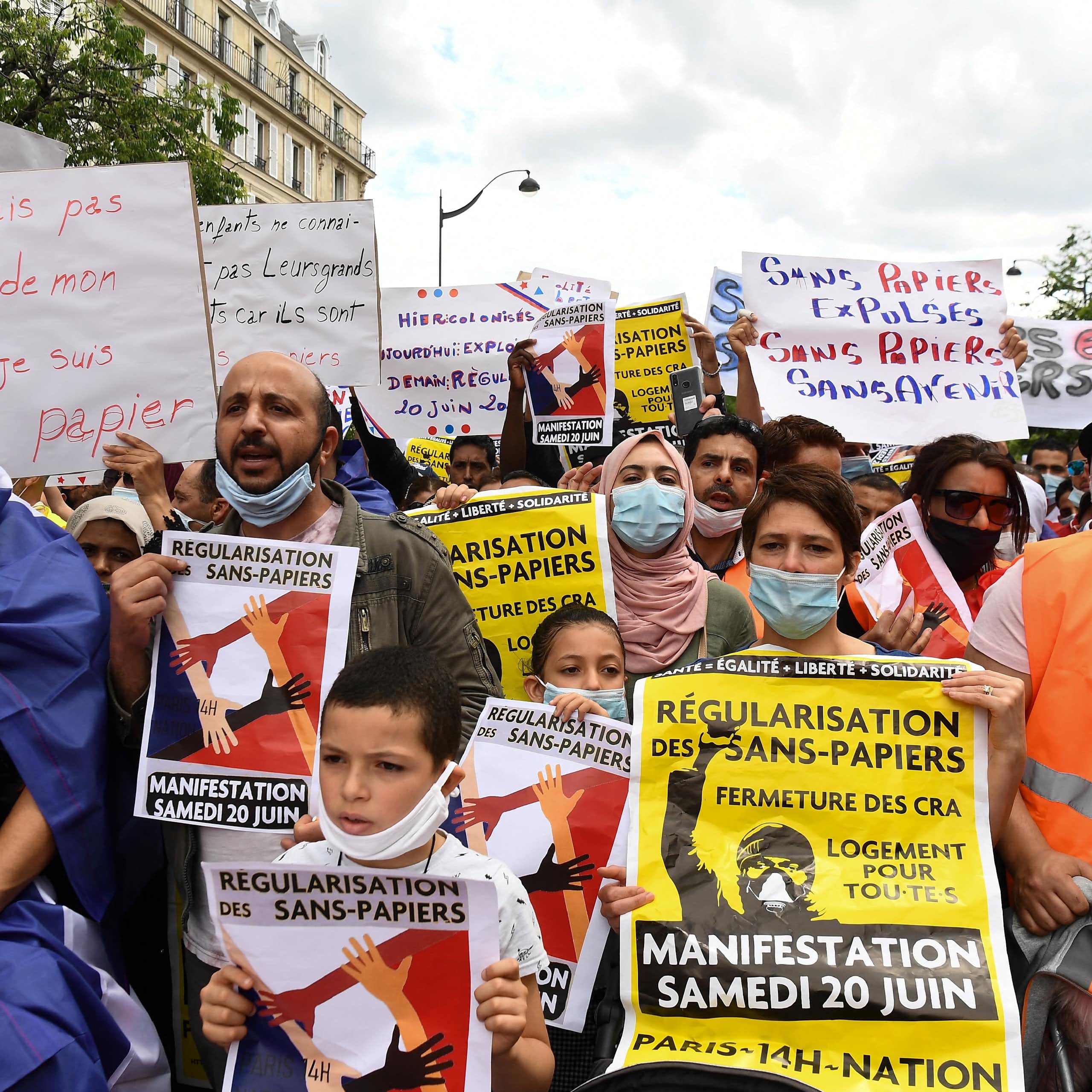 People hold signs with messages, written in French, calling for the regularisation of undocumented immigrants at a protest.