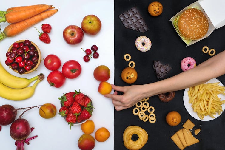 A person's hand reaches over an assortment of ultra-processed foods to chooses a minimally processed fruit instead.