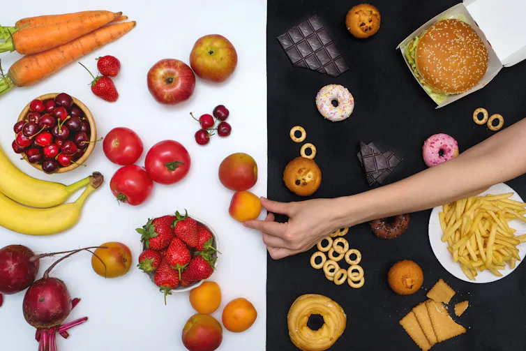 A person's hand reaches over an assortment of ultra-processed foods to chooses a minimally processed fruit instead.