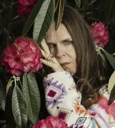 A woman posing betweenthe fronds of rhododendron blooms.