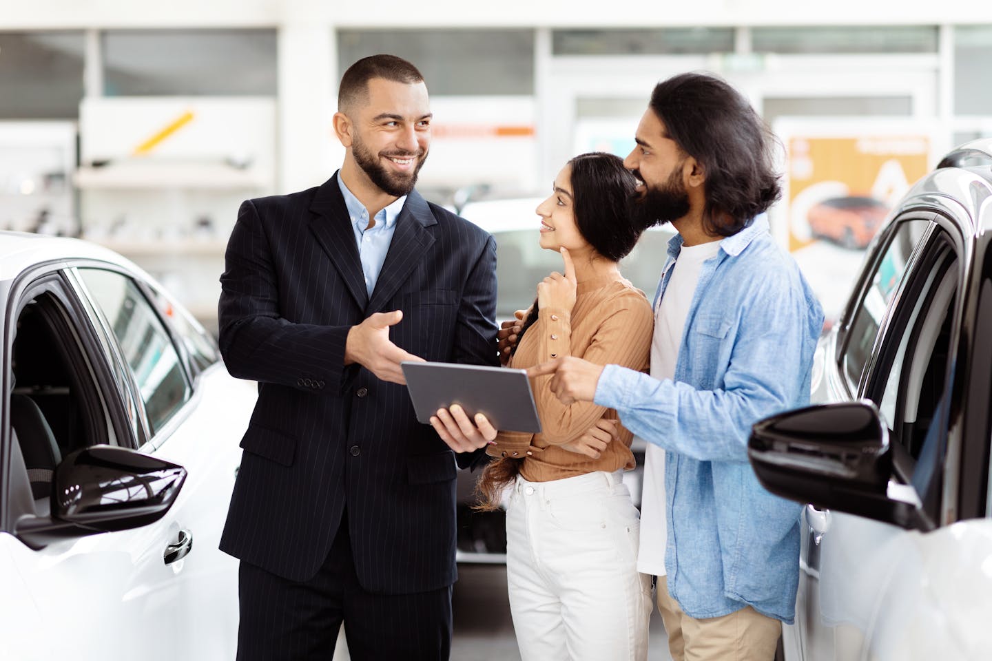 Car salesman holding tablet smiles at couple.