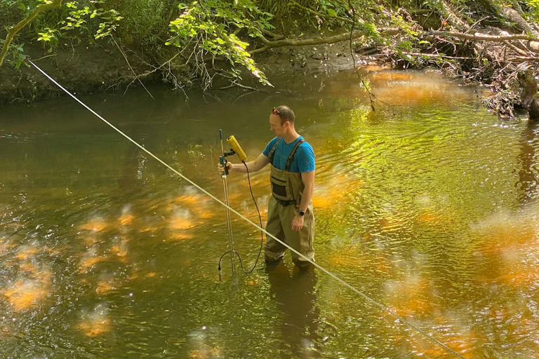 Man in waders holding sampling equipment standing in river