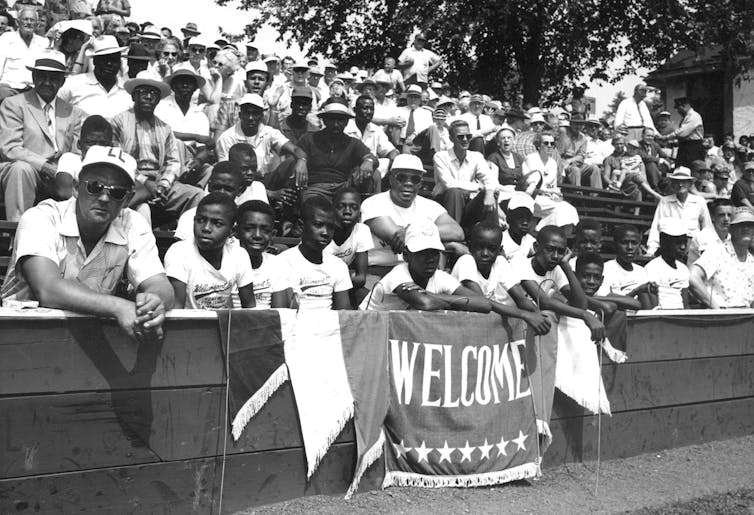 Black and white photo of Black boys and adults sitting in the stands at a baseball stadium.