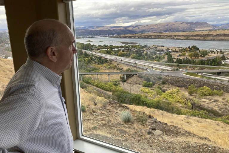 A man looks out a window at a river.