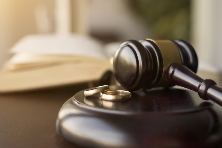 Two golden rings rest on a small wooden stand, with a judge's gavel on top, and an open book behind it.