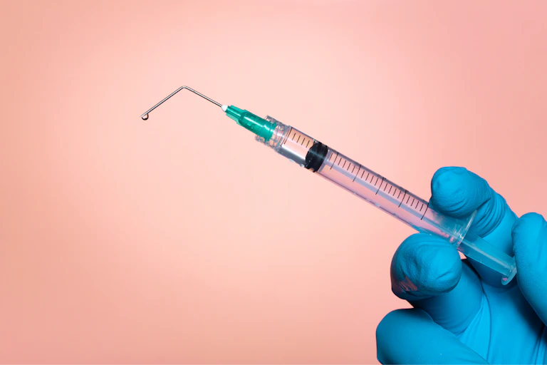 gloved hand squeezes syringe but the needle is bent