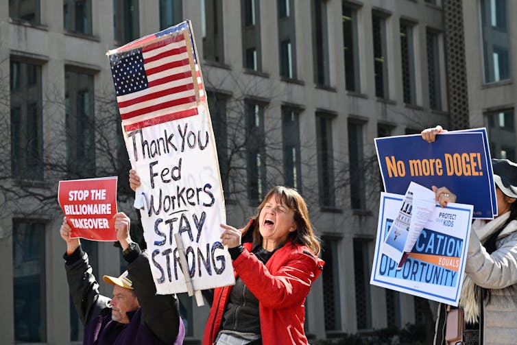 Protesters hold signs in solidarity with the American Federation of Government Employees outside of a big building.