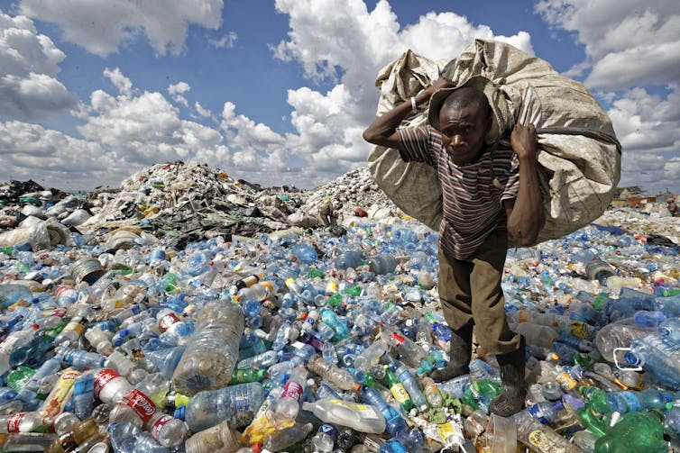 A man walks on a mountain of plastic bottles as he carries a sack of them to be sold for recycling after weighing them at the dump in the Dandora slum of Nairobi, Kenya.