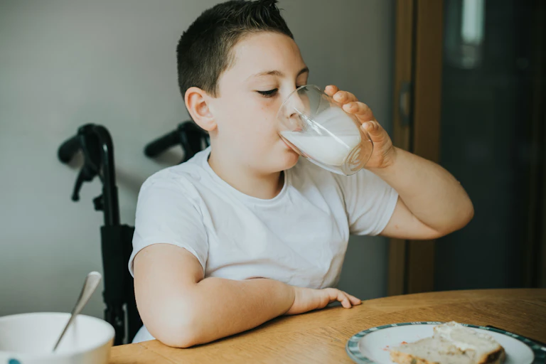 A child sitting at a table drinking a glass of milk