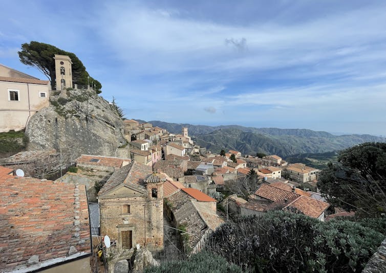 A mountain village in Calabria, Italy, with ancient houses and a church against a blue sky.