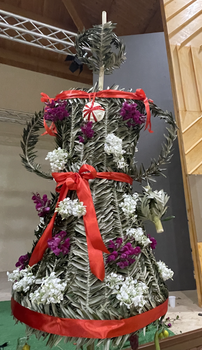 A decorated woven symbol of Persephone made of leaves, flowers and red ribbon.