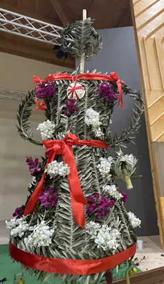 A decorated woven symbol of Persephone made of leaves, flowers and red ribbon.