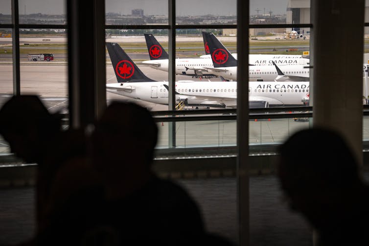 La gente pasa por una gran ventana, a través de la cual se pueden ver varios aviones de pasajeros en el aire de Canadá