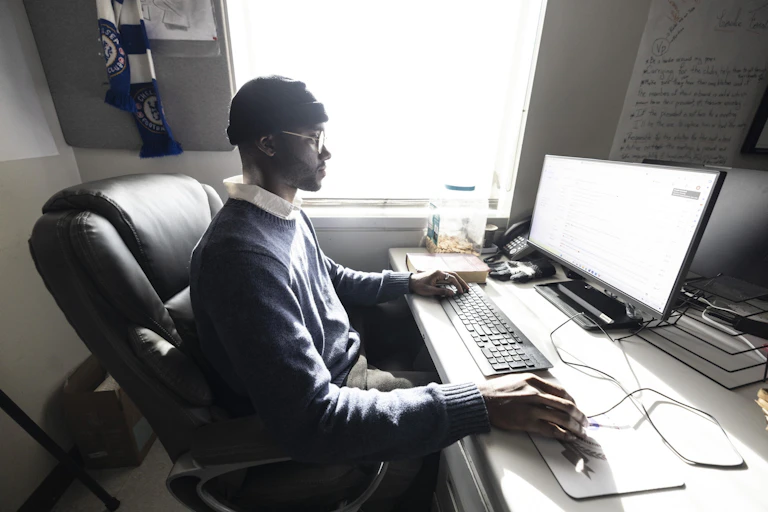 College student sitting at computer looking at large screen.