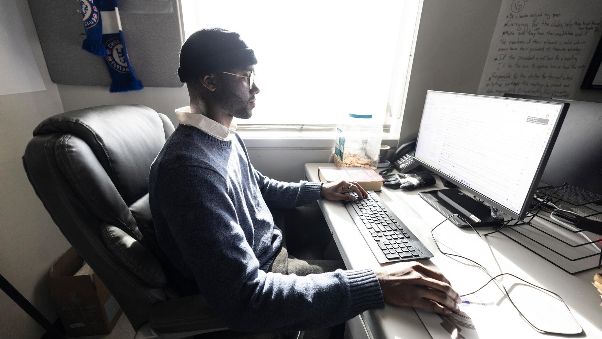 College student sitting at computer looking at large screen.