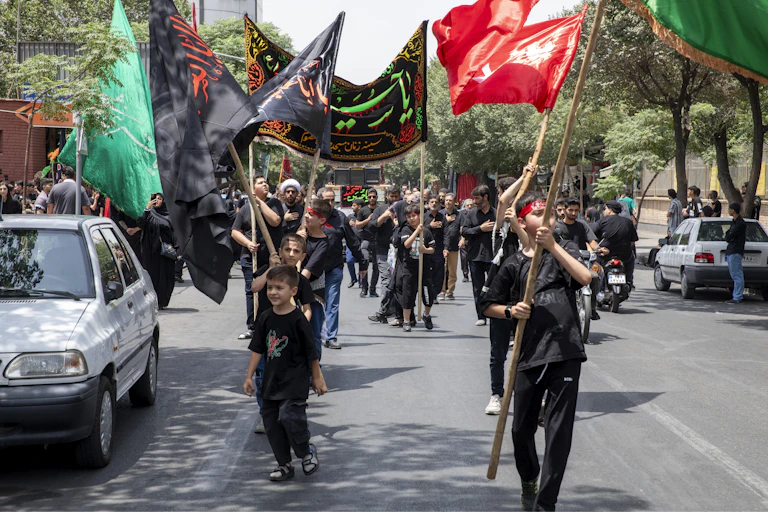 Participants dressed in black walk in procession, carrying large banners and flags in different colors.