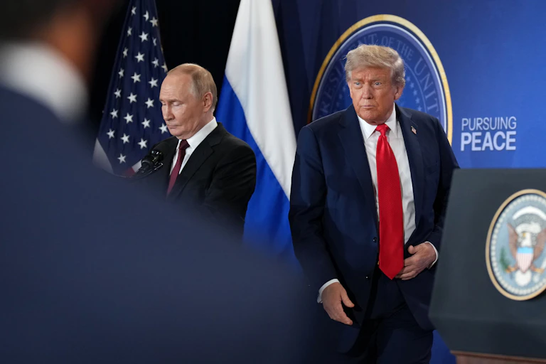 Two men in suits on a stage with two flags behind them.